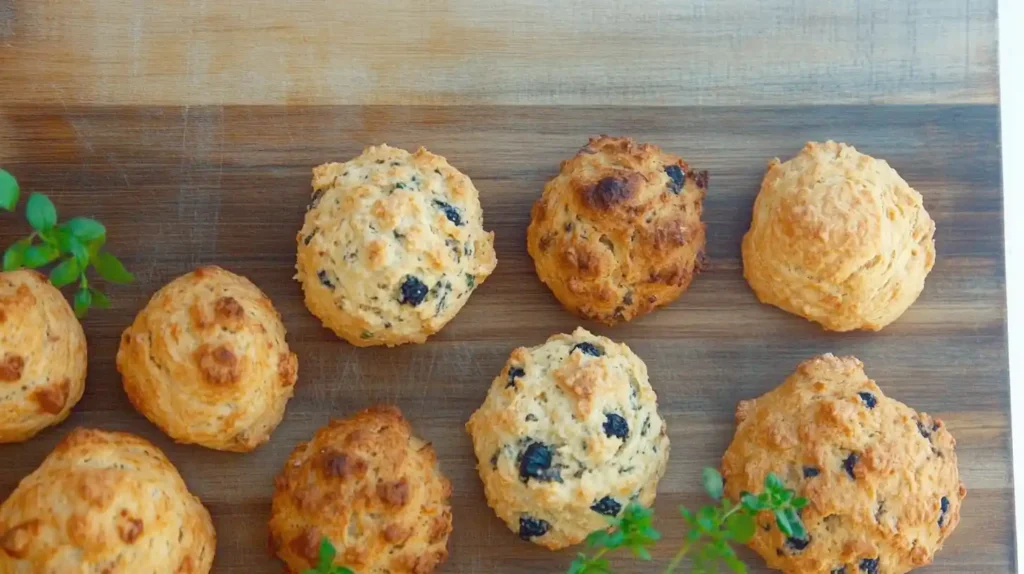 A selection of different scone flavors (blueberry, chocolate chip, cheddar herb) arranged on a rustic wooden board with decorative garnishes.