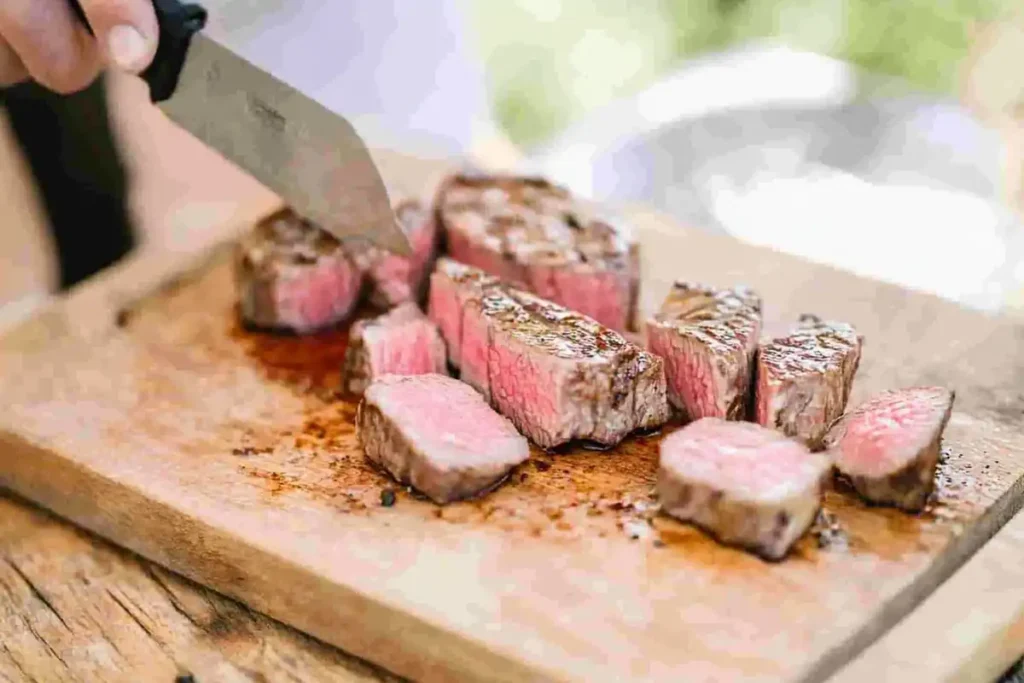 A close-up of a tender flank steak being sliced thinly on a wooden cutting board.