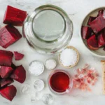 Fresh ingredients for making Fermented Beet Kvass arranged on marble surface including beets, water, salt, and starter culture