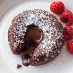 Molten chocolate lava cake with gooey center on white plate, dusted with powdered sugar and fresh raspberries